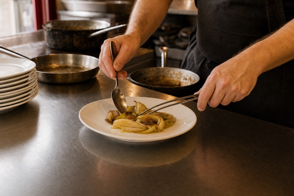 Manos emplatando en el pase de una cocina de acero inoxidable.